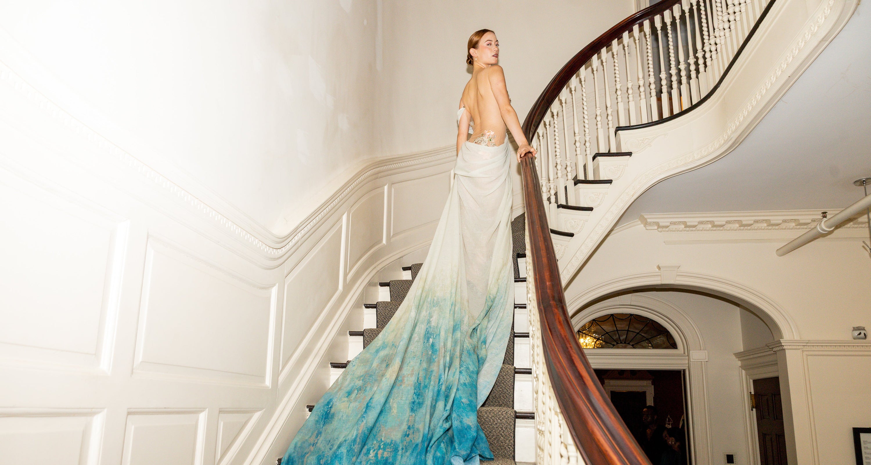 Woman in a long, elegant dress with a gradient from white to blue standing on a staircase.