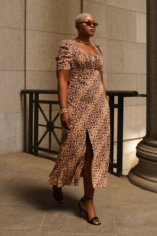 Woman in a leopard print dress standing against a stone wall.