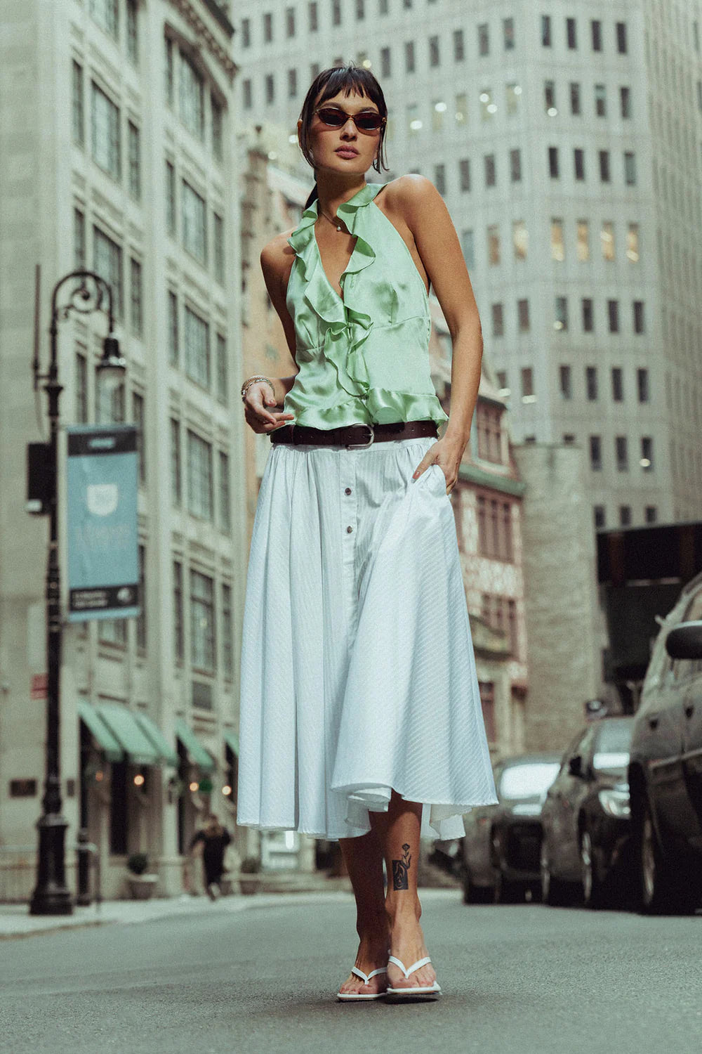 Woman in a mint green top and white skirt walking on a city street.