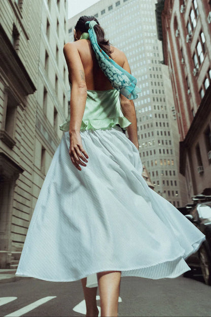 Woman in a light mint green top and white skirt walking on a city street.
