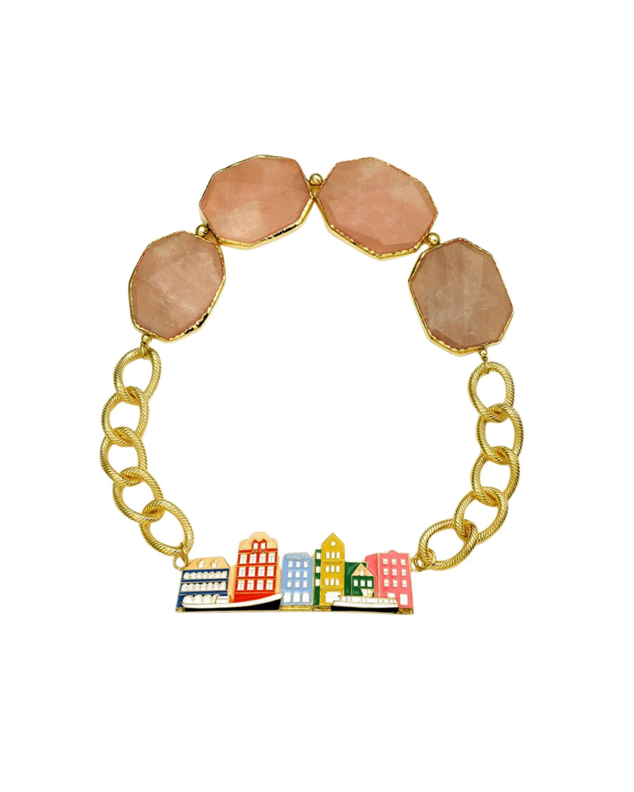 A gold chain bracelet featuring four peach-pink faceted gemstone beads at the top and a colorful cityscape charm with miniature buildings in red, yellow, blue, green, and white at the bottom, set against a plain white background.